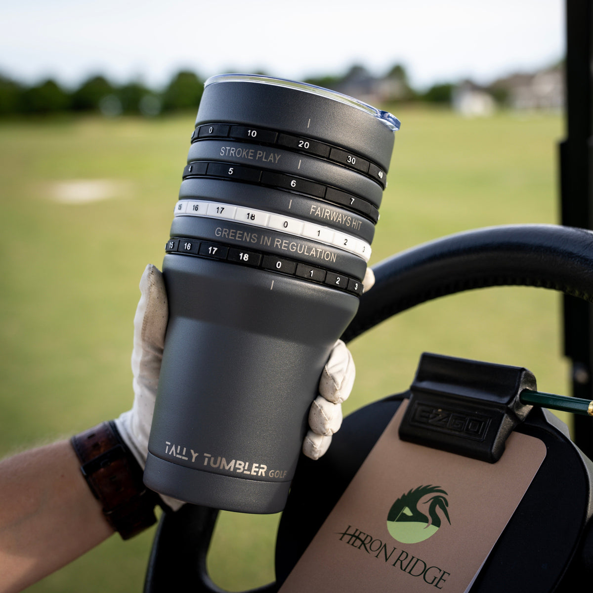 Person holding a gray tumbler with a golf cart and grassy area in the background